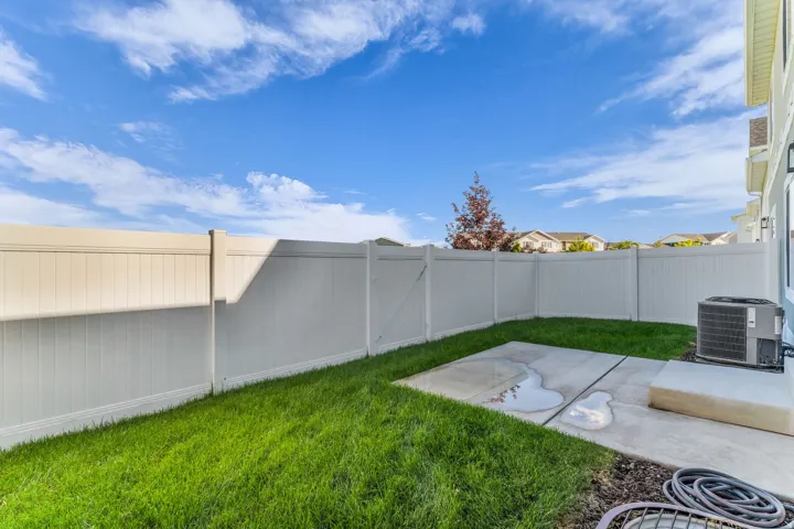 Enclosed backyard featuring a concrete patio, green lawn, and privacy fencing