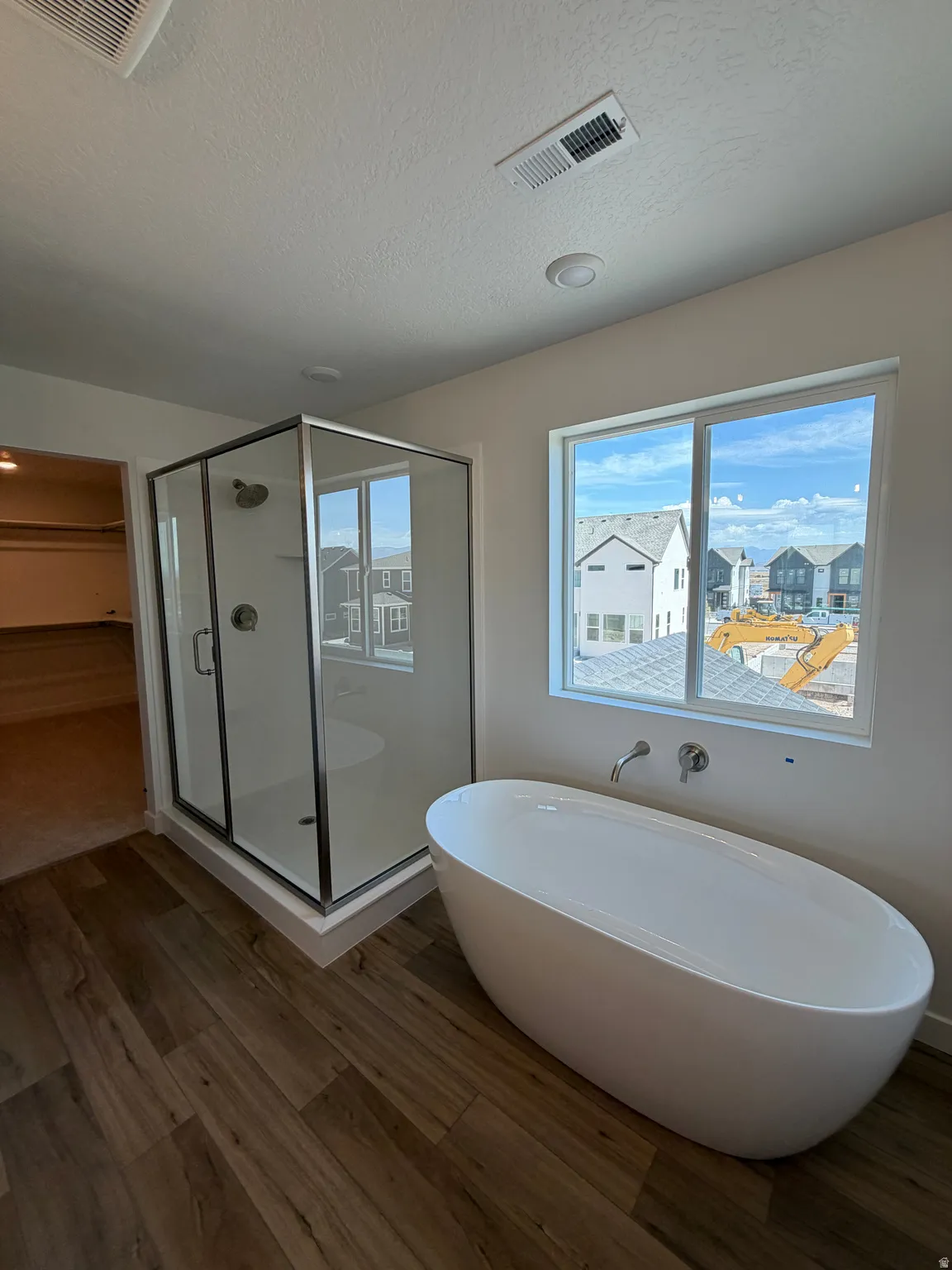 Grand Primary Bathroom featuring freestanding soaking tub, glass-enclosed shower, wood-finish flooring, and recessed lighting