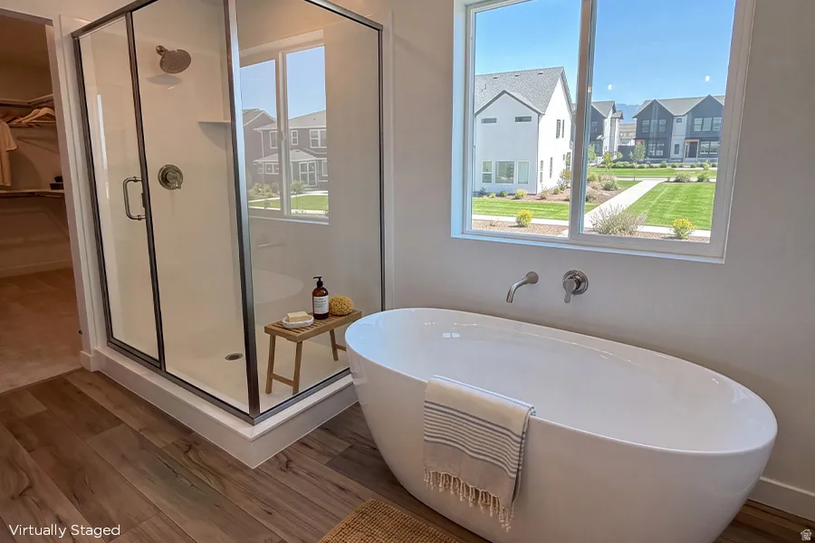 Freestanding soaking tub with wall-mounted fixtures, glass-enclosed shower, and wood-finish flooring