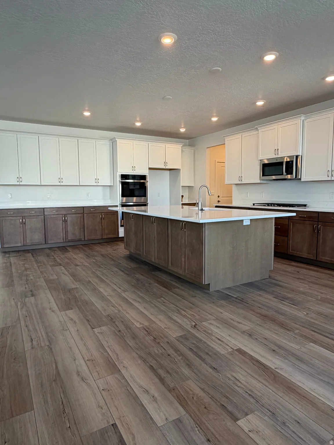 Expansive kitchen featuring two-tone cabinetry, a large central island with seating, stainless steel appliances, and recessed lighting