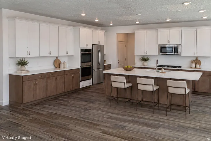 Spacious kitchen featuring an expansive island, stainless steel appliances, wood-finish flooring, two-tone cabinetry, and recessed lighting