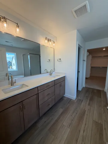 Primary Bedroom bathroom. Dual sink vanity with white countertop, wood-finish flooring, and contemporary lighting fixtures