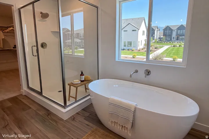 Freestanding soaking tub with wall-mounted fixtures, glass-enclosed shower, and wood-finish flooring