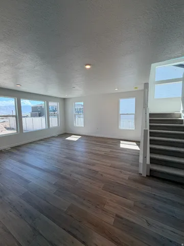 Spacious room featuring wood-finish flooring, recessed lighting, multiple large windows, and a carpeted staircase with a white railing