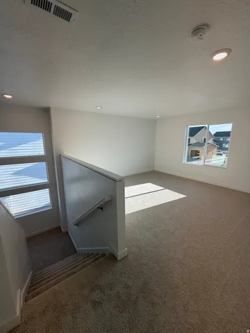 Carpeted living area with abundant natural light from multiple windows and recessed ceiling lighting