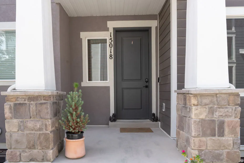 Entryway featuring a dark paneled door, stone-clad columns, stucco siding, and a concrete porch