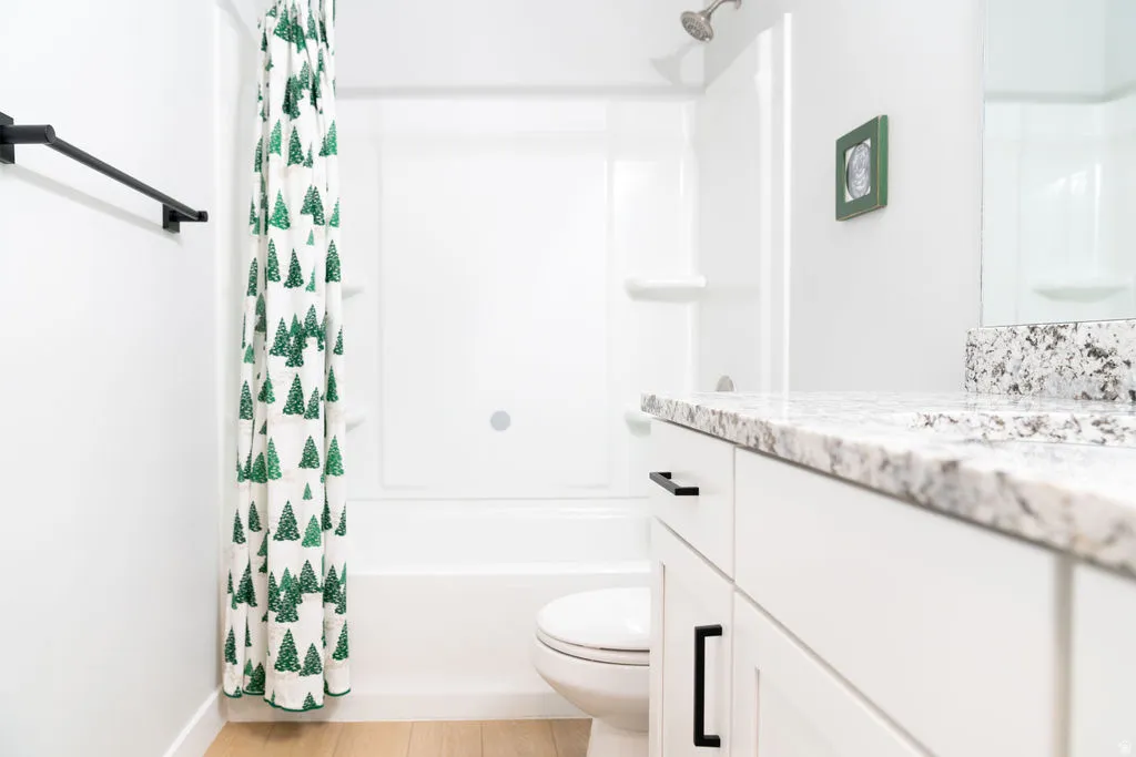 White vanity with black hardware, speckled countertop, white shower/tub combination, and light wood-finish flooring