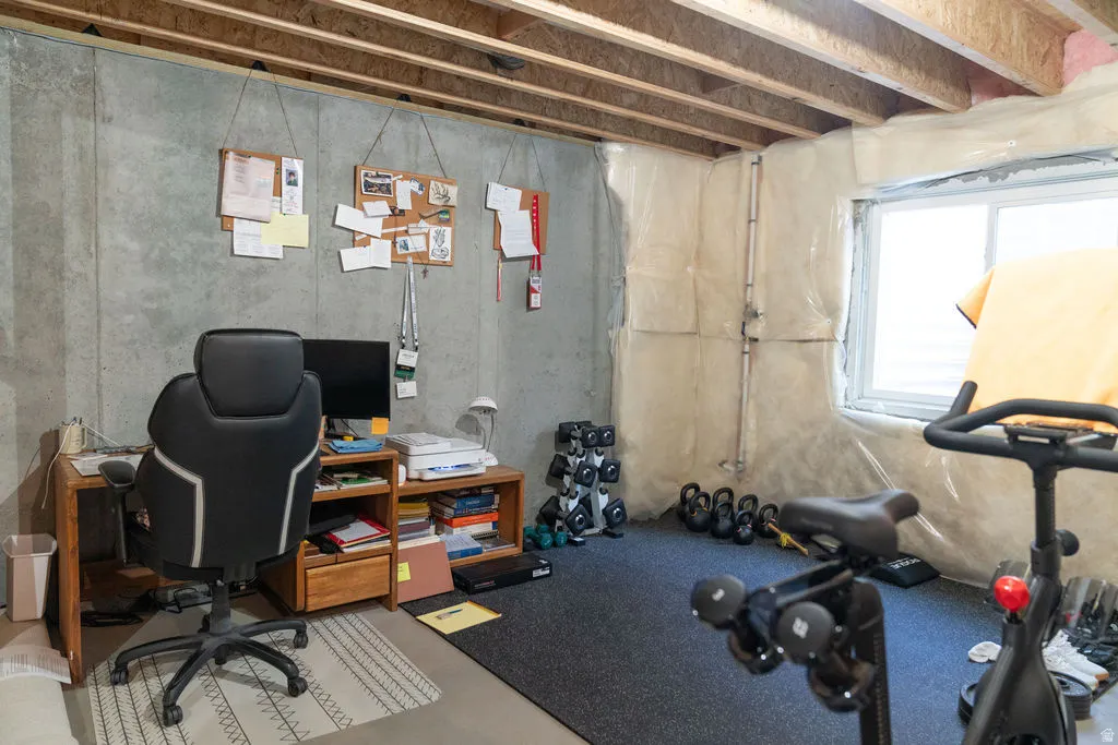 Unfinished basement space featuring exposed concrete walls, exposed ceiling joists, and a window for natural light