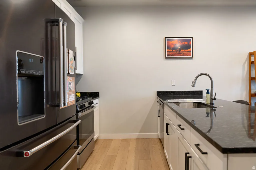 Modern kitchen featuring stainless steel appliances, dark countertops, white cabinetry, and wood-finish flooring