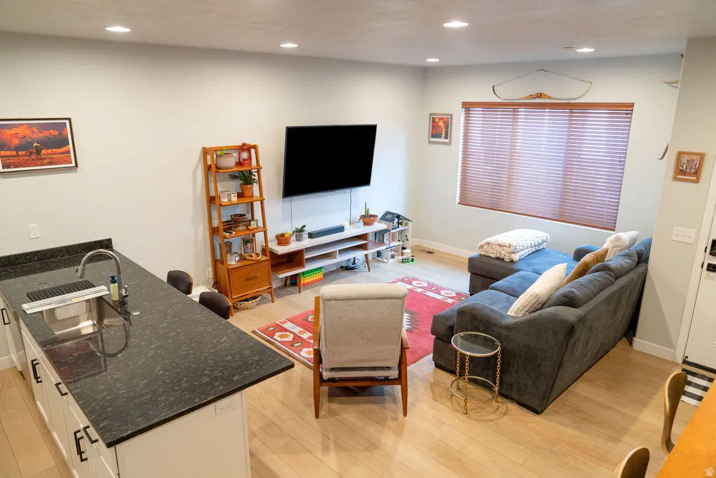 Open-concept living space featuring wood-finish flooring, recessed lighting, and a kitchen island with a built-in sink and dark stone-finish countertop