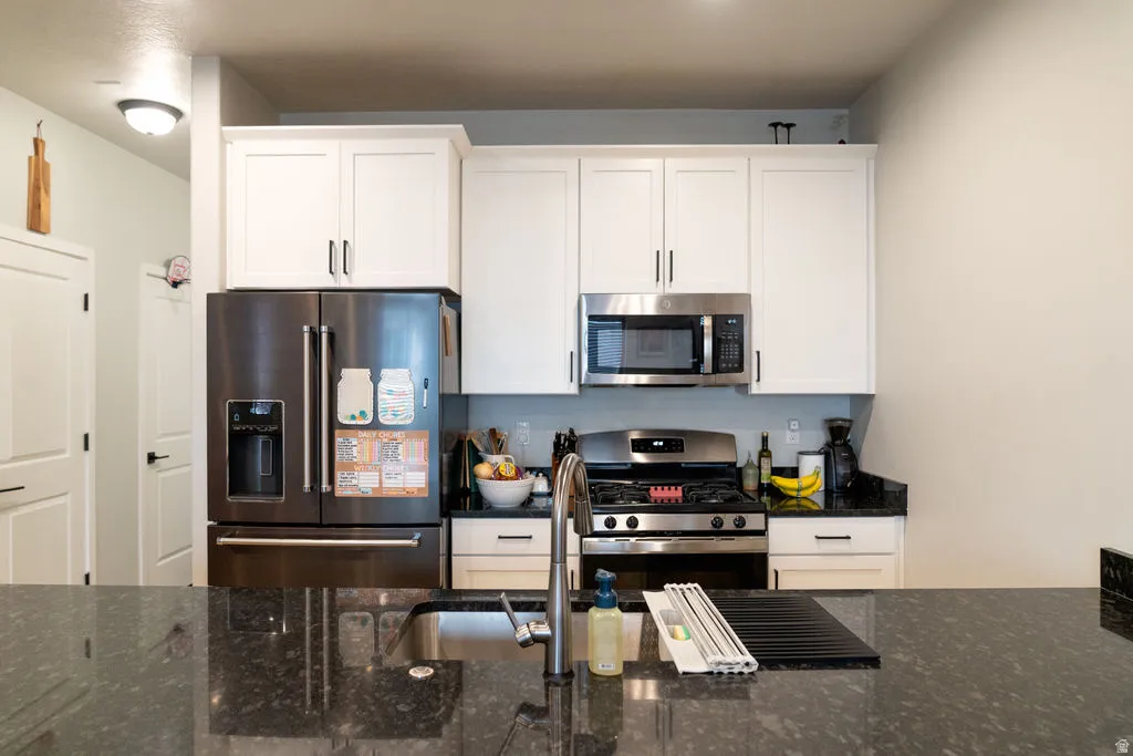 Kitchen featuring a stainless steel refrigerator, microwave, and range, white shaker-style cabinetry, and dark granite countertops