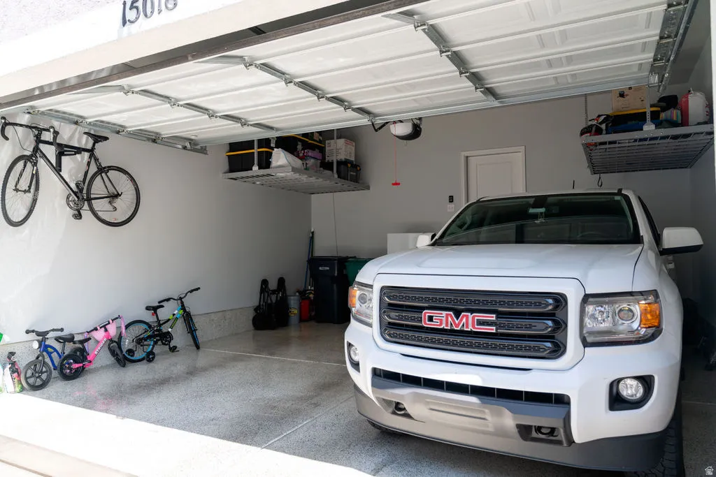 Attached garage with a white sectional door, concrete flooring, and overhead storage racks