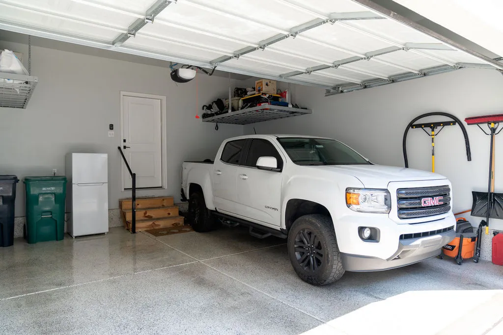 Attached garage featuring a durable epoxy floor, overhead storage racks, a white paneled entry door, and a garage door opener