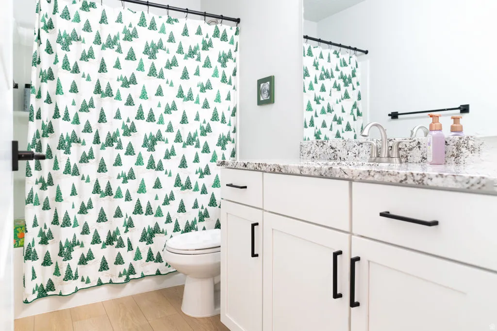 White vanity with black hardware, stone-finish countertop, and wood-finish flooring