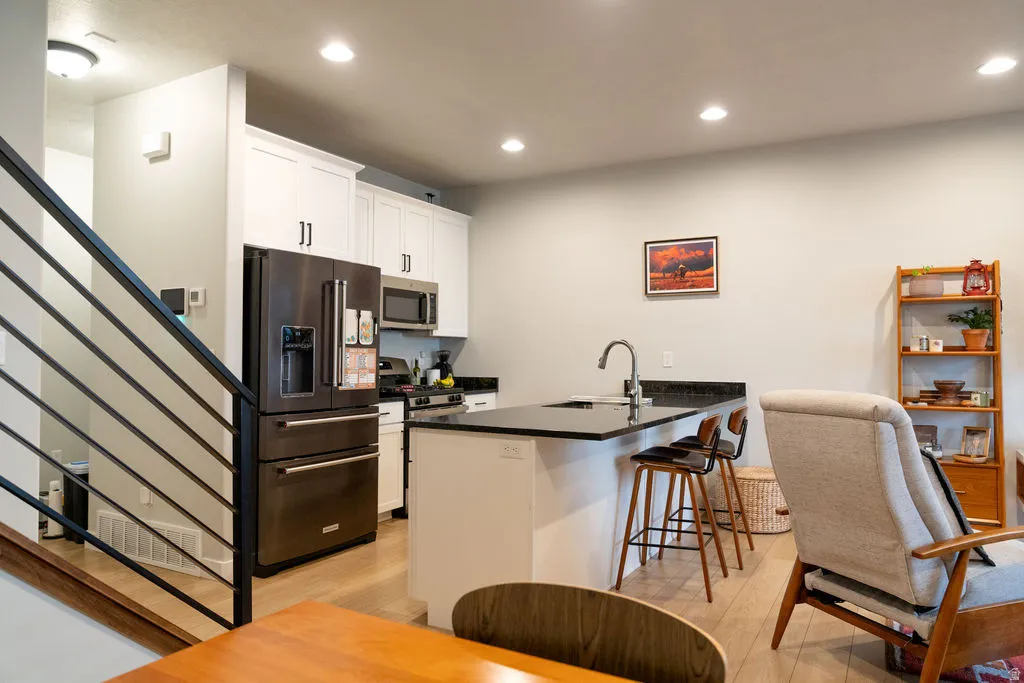 Kitchen featuring white cabinetry, stainless steel appliances, dark countertops, and an island with a built-in sink