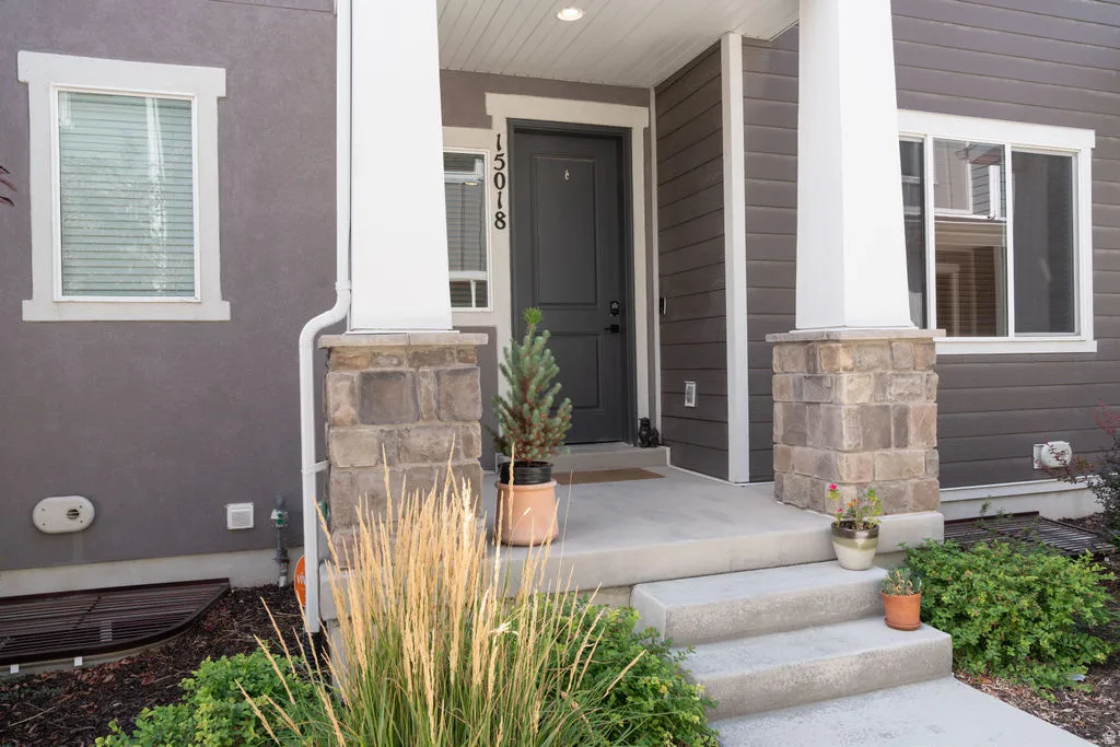 Entryway with a dark gray door, concrete steps, and stone-clad pillars
