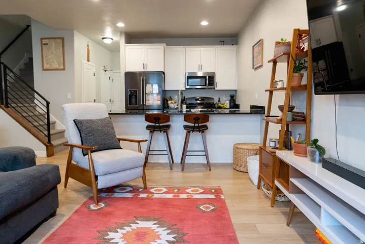 Open-concept living area with wood-finish flooring, a kitchen featuring white cabinetry and stainless steel appliances, and a staircase with a wood handrail and metal balusters