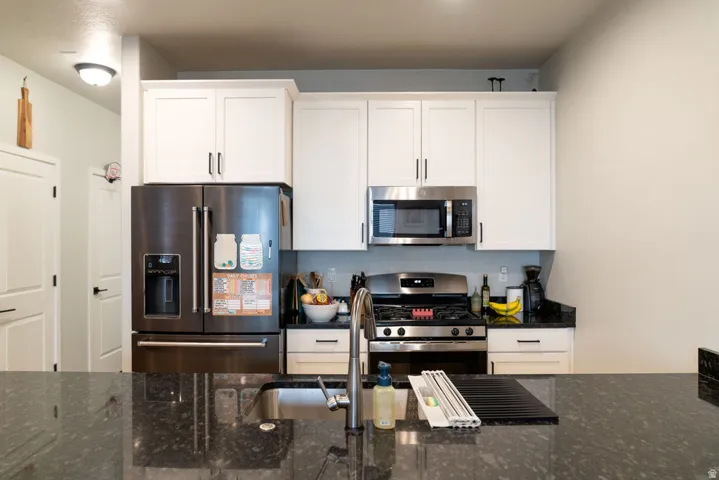 Kitchen featuring a stainless steel refrigerator, microwave, and range, white shaker-style cabinetry, and dark granite countertops