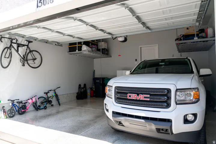 Attached garage with a white sectional door, concrete flooring, and overhead storage racks