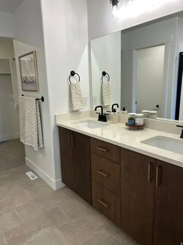 Dual vanity with undermount sinks, wood-finish cabinetry, light-toned countertop, and matte black fixtures