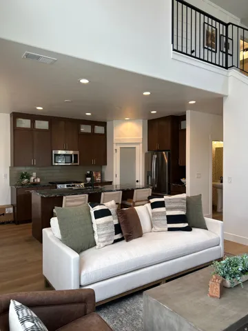 Open-concept living space featuring a high ceiling, wood-finish flooring, and a kitchen with dark cabinetry, stainless steel appliances, and an island with bar seating
