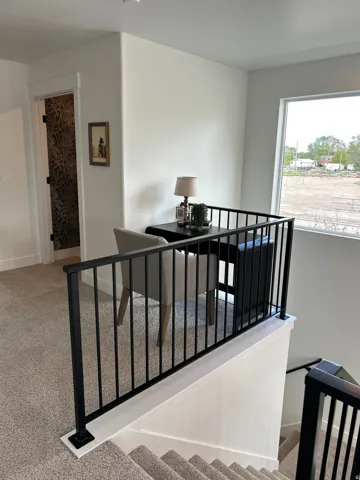 Loft area with a large window, black metal railing, and carpeted flooring