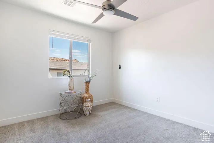 Bright secondary bedroom offering neutral carpet flooring, ceiling fan with integrated lighting, and large window framing natural daylight and distant landscape vistas