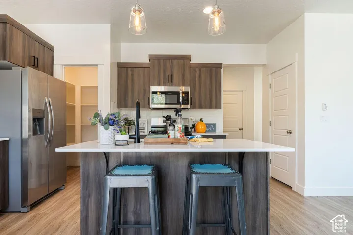 Kitchen featuring wood-finish flooring, stainless steel appliances, a center island with countertop seating, and recessed and pendant lighting