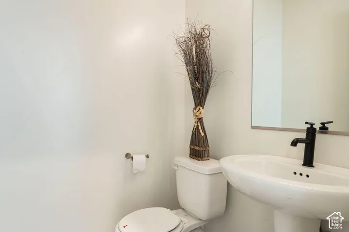White pedestal sink with a matte black faucet, a toilet, and a wall-mounted mirror