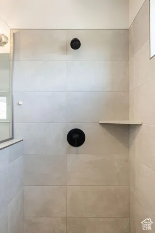 Walk-in shower featuring large format tile, matte black shower fixtures, and a built-in shower shelf