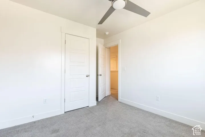 Bright secondary bedroom featuring neutral carpeting, white panel doors, and ceiling fan for climate control
