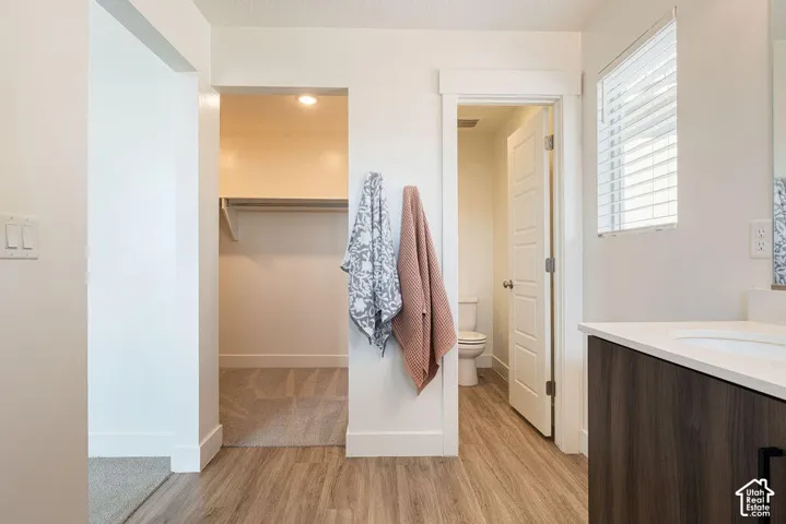 Wood-finish flooring, built-in shelving, white walls, window with blinds, and a built-in vanity with white countertop