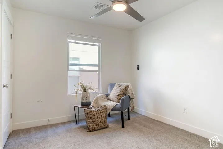Bright, naturally lit bedroom featuring large windows, neutral carpeting, ceiling fan with integrated lighting, and clean white walls ideal for personalization