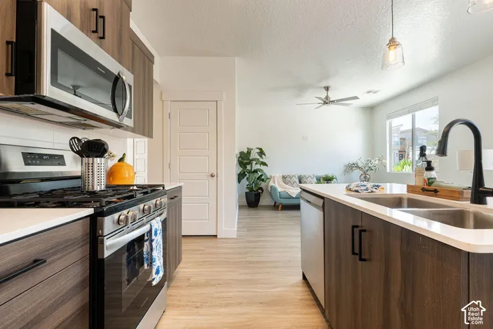 Stainless steel appliances, wood-finish flooring, white countertops, dark wood-finish cabinetry, and a ceiling fan