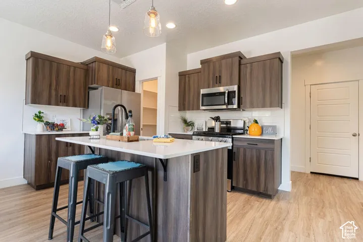 Wood-finish cabinetry, white countertops, stainless steel appliances, white subway tile backsplash, and wood-finish flooring
