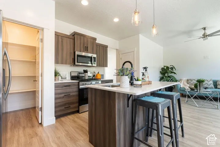 Kitchen featuring wood-finish cabinetry, stainless steel appliances, a center island with counter seating, and a pantry with shelving