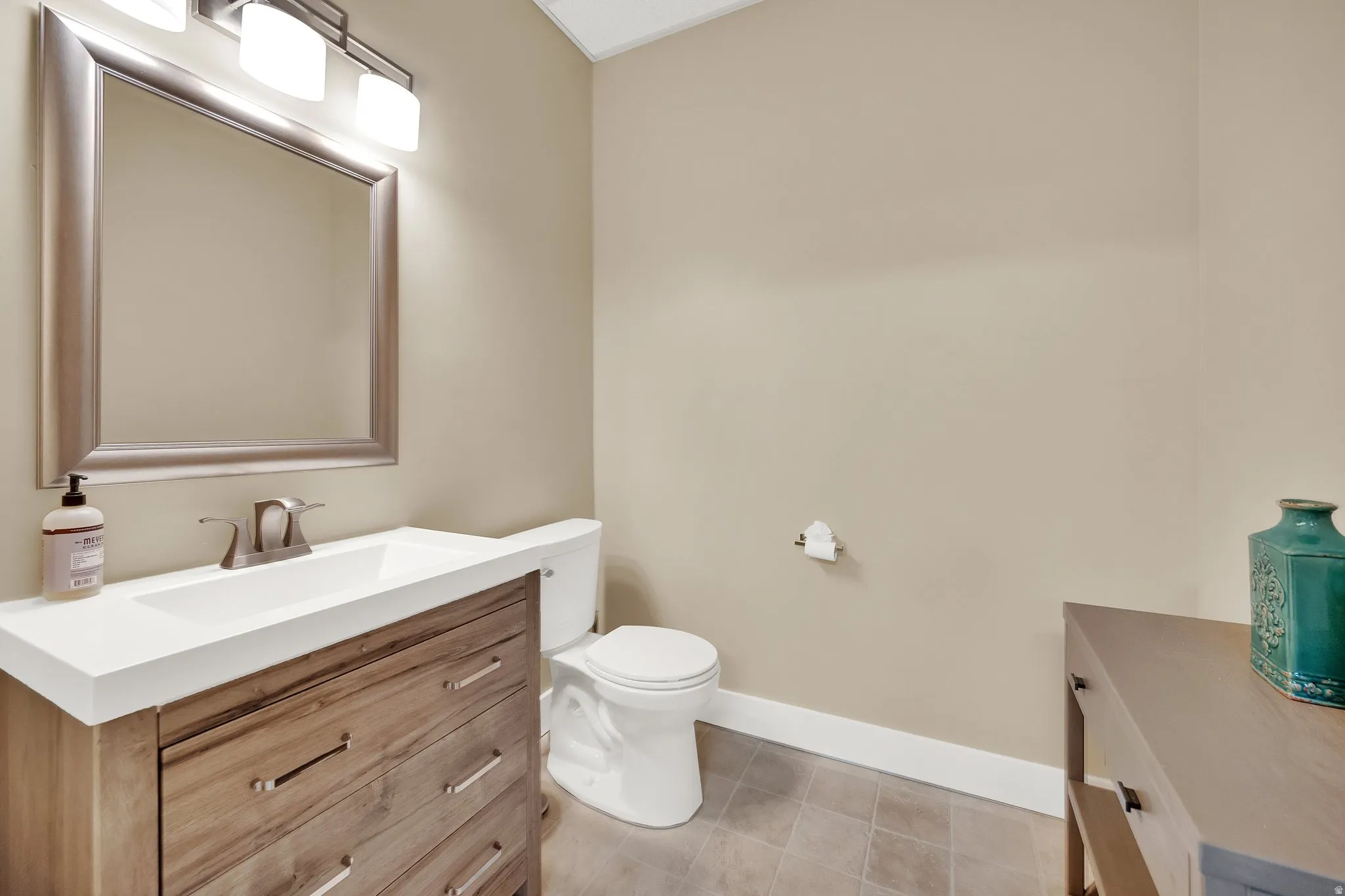 Vanity with a wood-finish cabinet and integrated sink, brushed nickel faucet, framed mirror, and wall-mounted light fixture