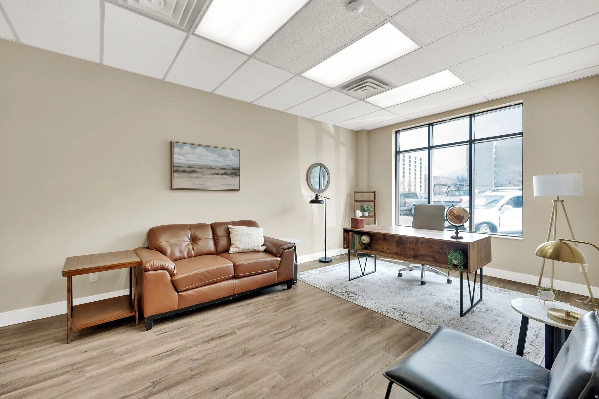 Spacious room with large windows, wood-finish flooring, drop ceiling with integrated lighting, and neutral wall tones