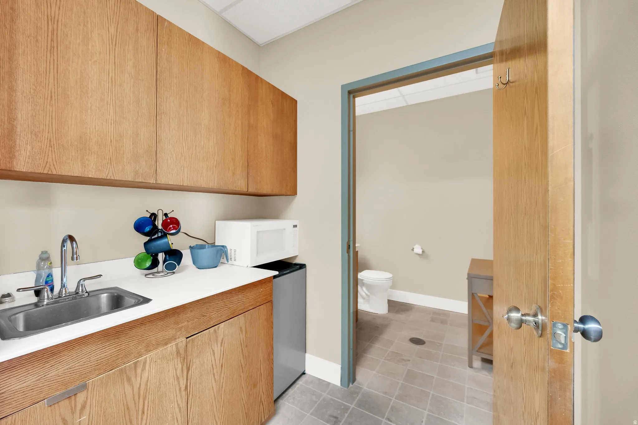 Integrated kitchenette with wood-finish cabinetry, stainless steel sink, and light-toned countertops