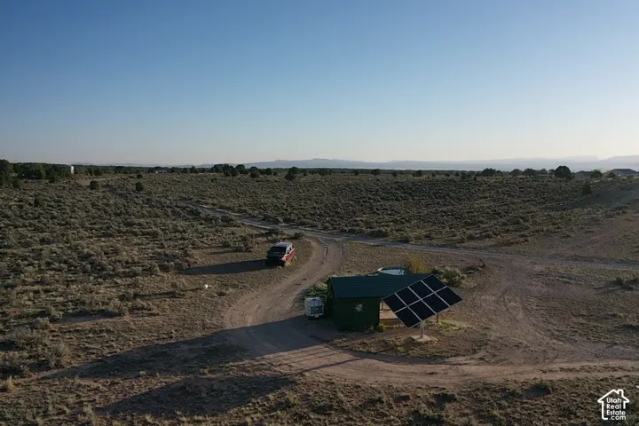Expansive land featuring a structure with a dark roof, solar panel array, and a dirt access road