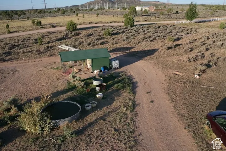Green shed structure with an attached covered porch, large circular water trough, and unpaved access road