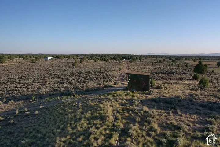 Expansive, arid landscape featuring natural vegetation, scattered trees, and a distant structure
