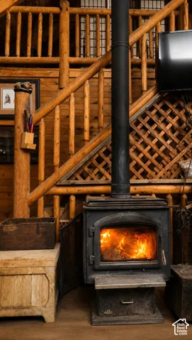 Cast iron wood stove with a black stovepipe, wood-paneled walls, and a wood staircase with rustic log railings