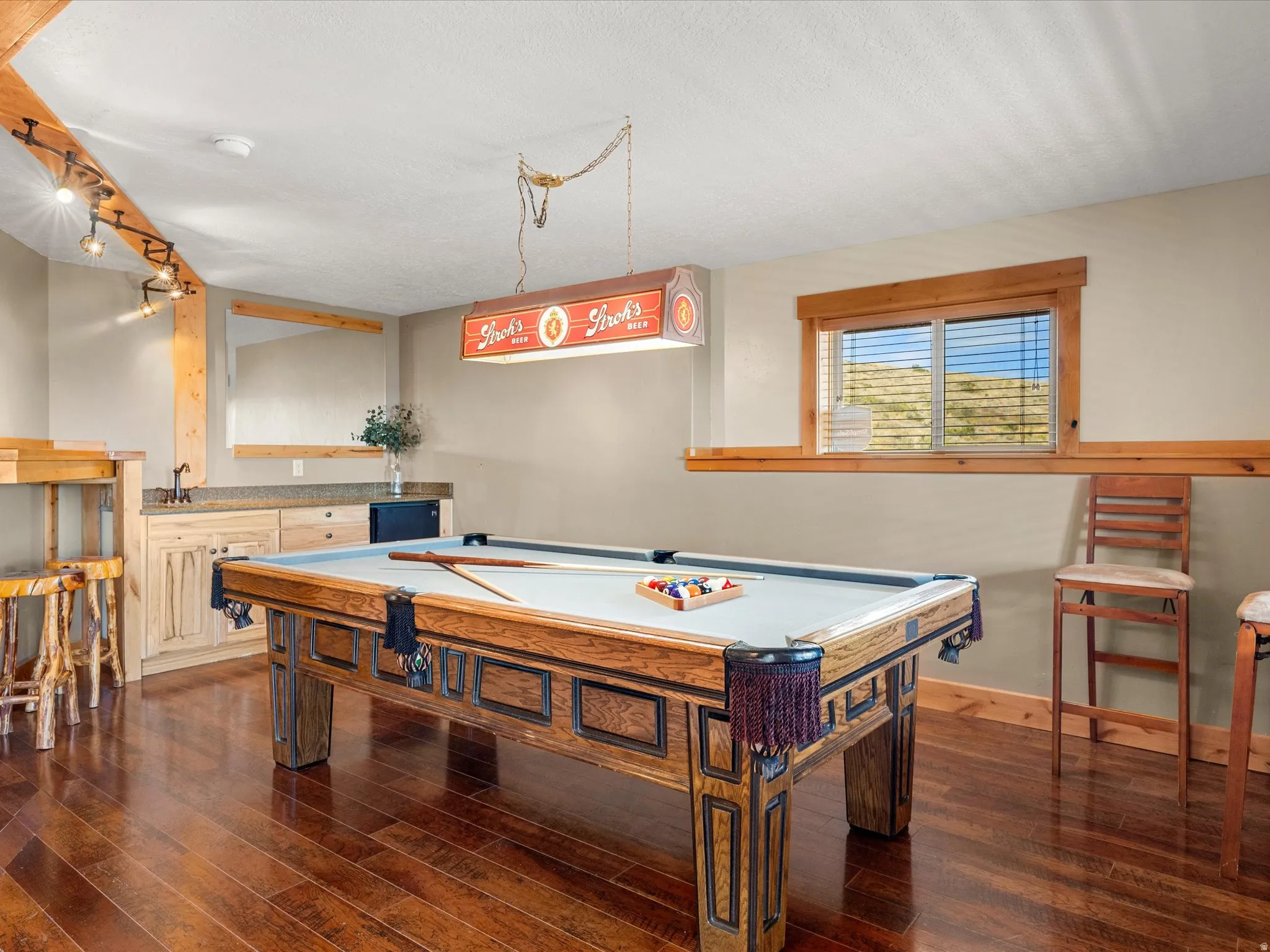 Wood-finish flooring, built-in wet bar with stone countertop, track lighting, and a window with natural light