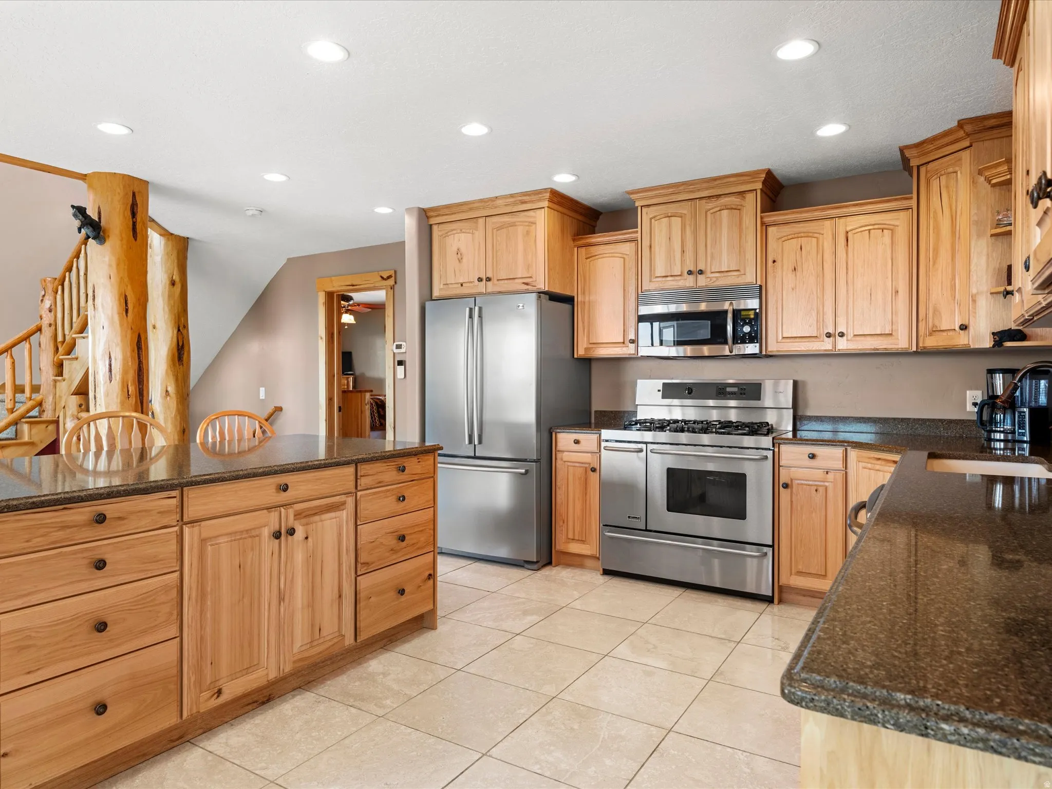 Kitchen featuring stainless steel appliances, wood cabinetry, stone countertops, and tile flooring