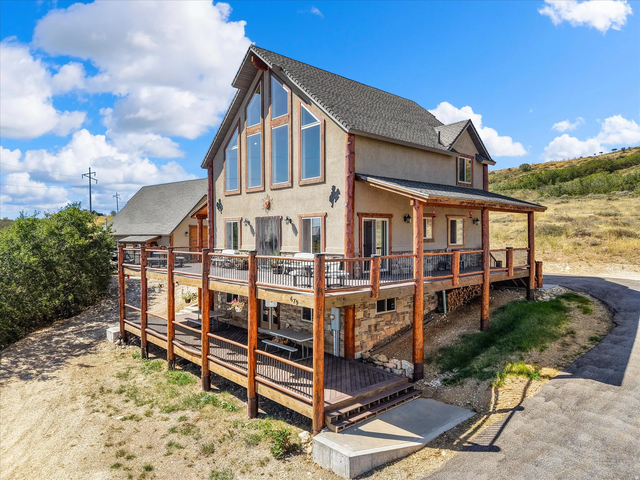 Multi-level deck with wood-finish railings, extensive exterior glazing, stucco siding, stone accents, and a covered porch