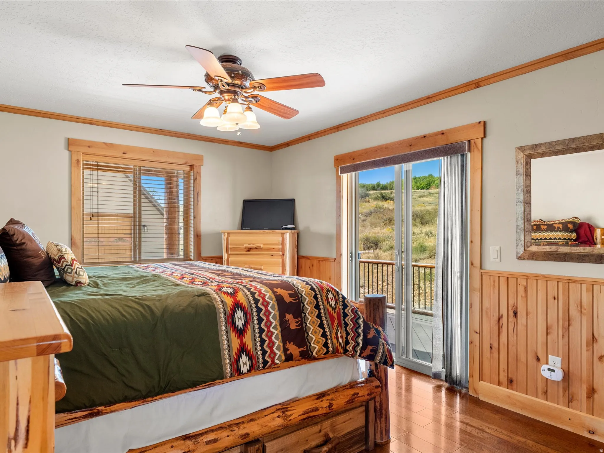 Hardwood flooring, wood paneling, sliding glass door with balcony, ceiling fan with integrated lighting, and wood-trimmed window
