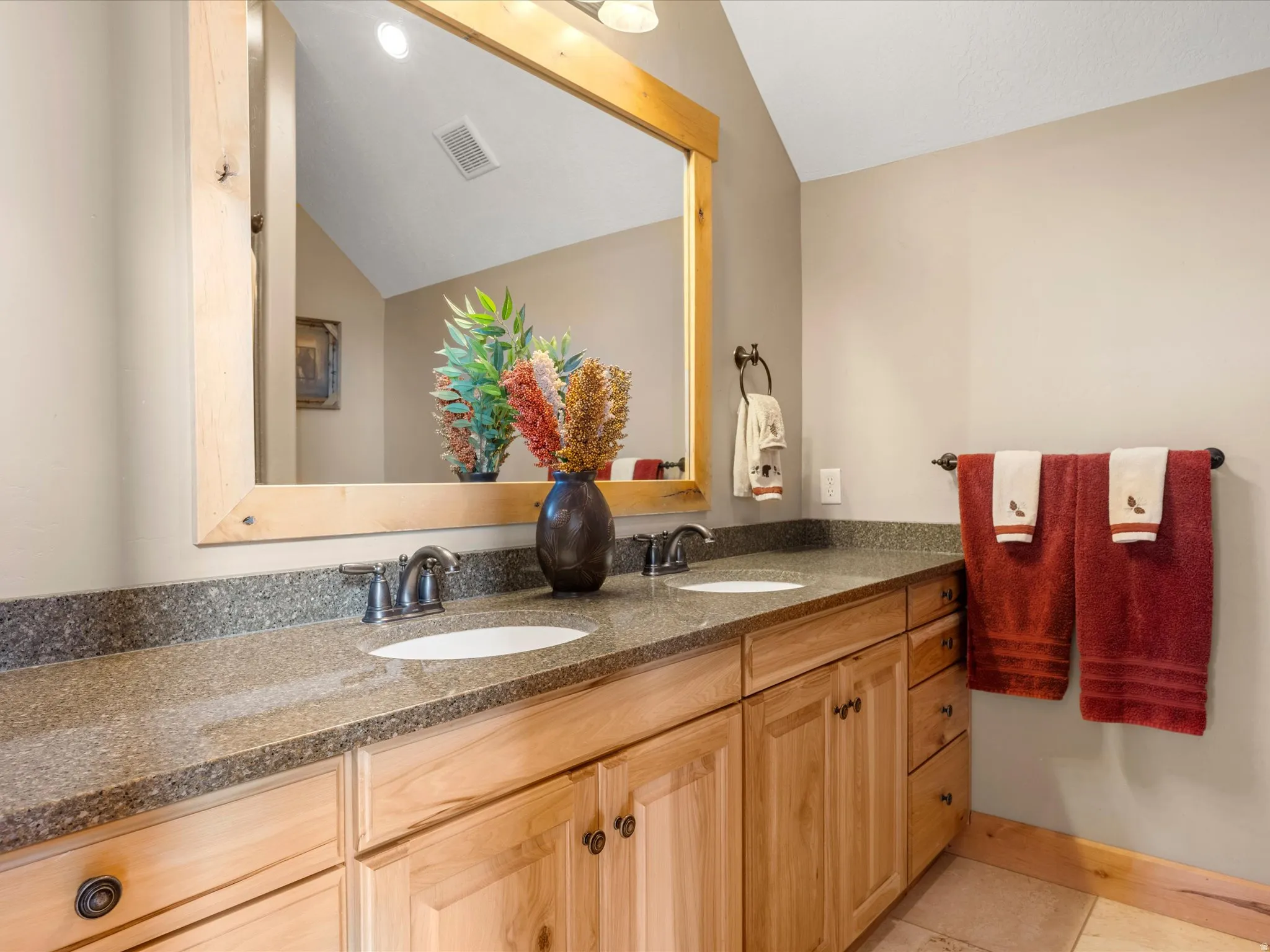 Double vanity with light wood cabinetry, stone-finish countertop, and undermount sinks