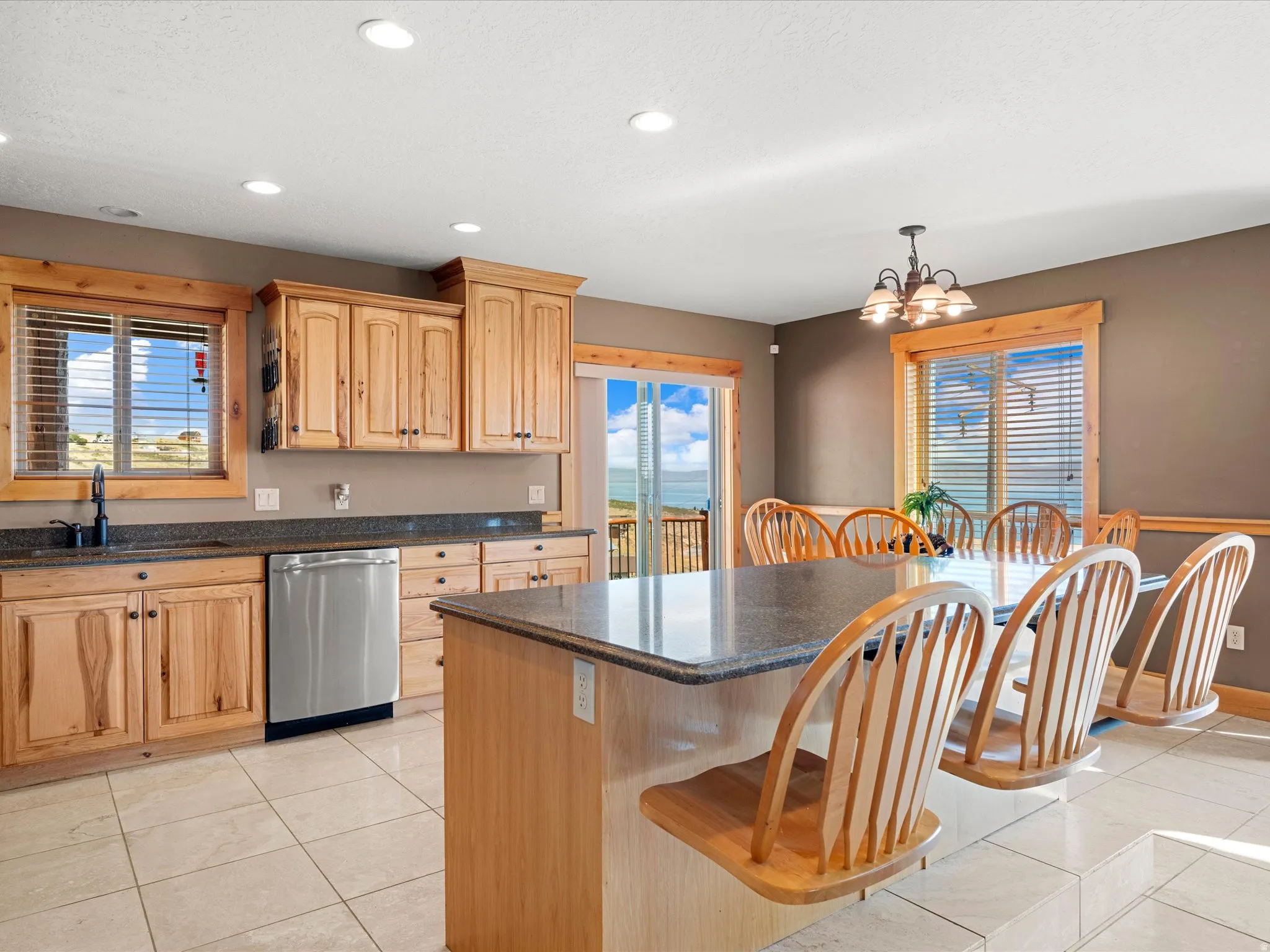 Recessed lighting, wood cabinetry, stainless steel dishwasher, dark stone countertops, and tile flooring