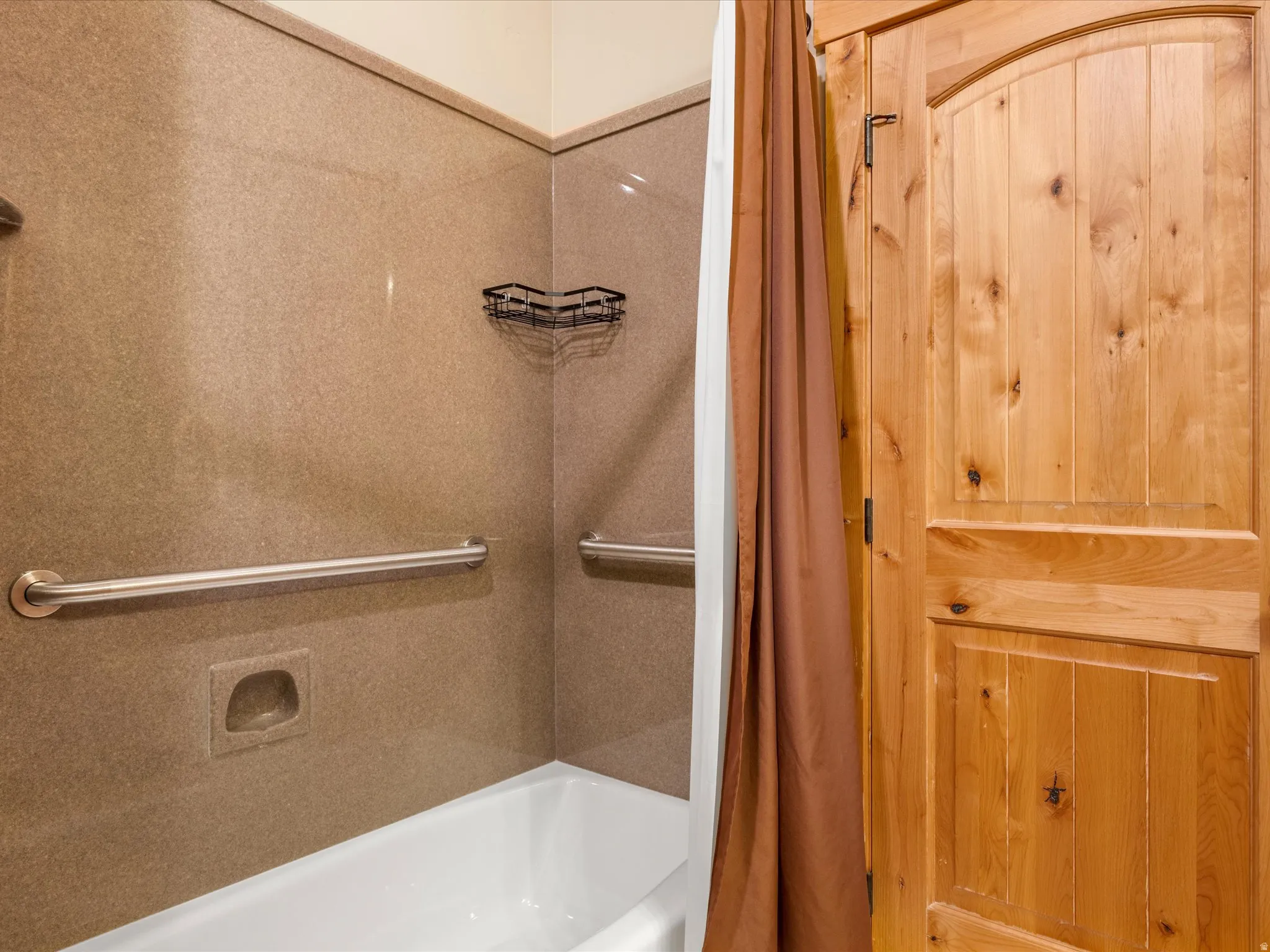 Tub/shower combination featuring a light-colored surround, grab bars, and a built-in soap dish